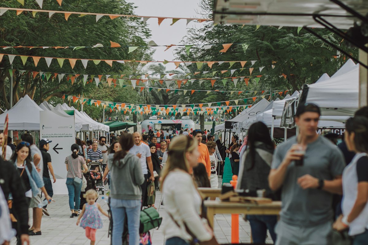 Visitors walking between vendor tents strung with bunting at an outdoor community festival.