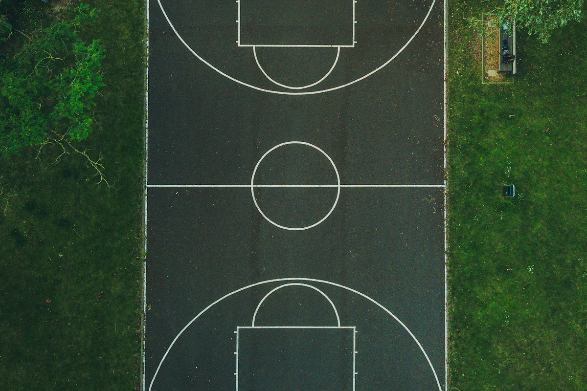 An overhead view of a marked outdoor basketball court bordered by grass.