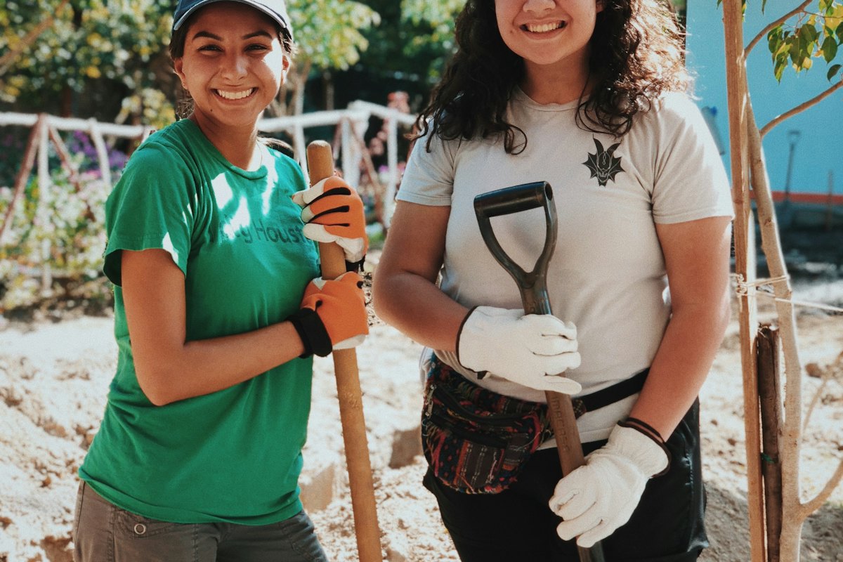 Two volunteers in work gloves holding shovels at an outdoor planting site.